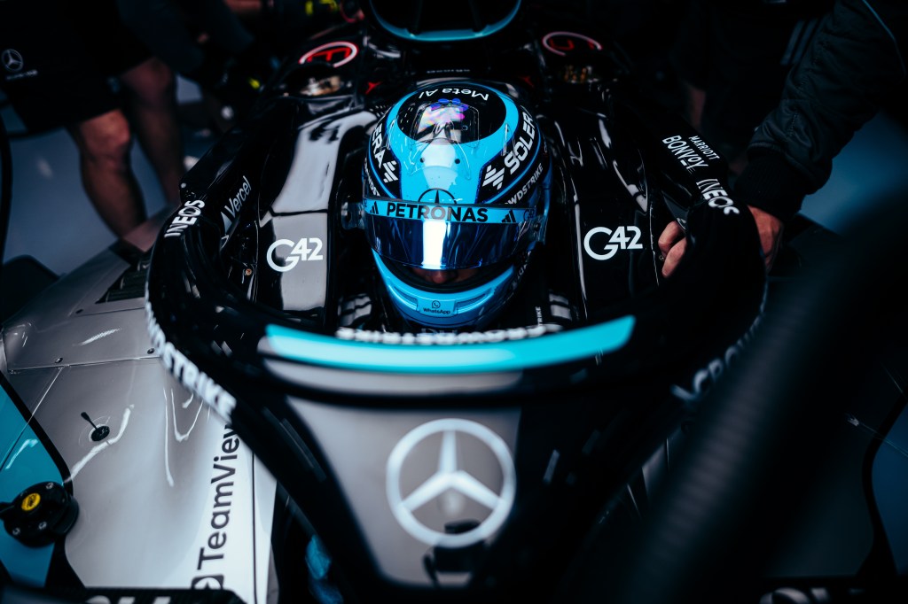 Formula 1 driver seated in a Mercedes race car while the pit crew prepares the vehicle in the garage.